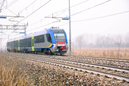 Téléchargez les photos : Train de banlieue se déplaçant à travers la campagne par un matin d'hiver brumeux - en image libre de droit