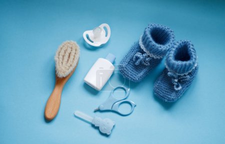 Baby boy accessories background, booties, tiny rod, soother, brush, and toys over blue background with copy space, top view. Concept of Infancy and motherhood