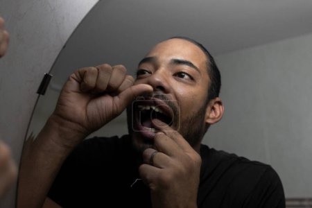 Téléchargez les photos : Colombien homme fil dentaire tout en se regardant dans le miroir - en image libre de droit