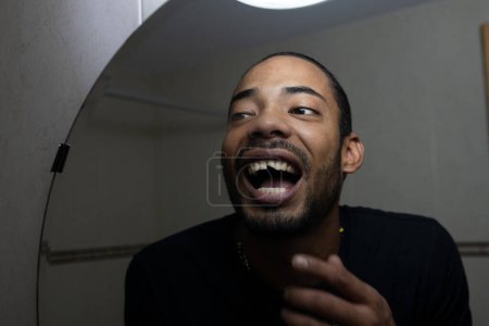 Téléchargez les photos : Latin homme regardant son sourire avec une dent cassée - en image libre de droit