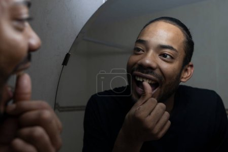 Téléchargez les photos : Latin guy toucher sa dent cassée avec sa main tout en le regardant dans le miroir. - en image libre de droit