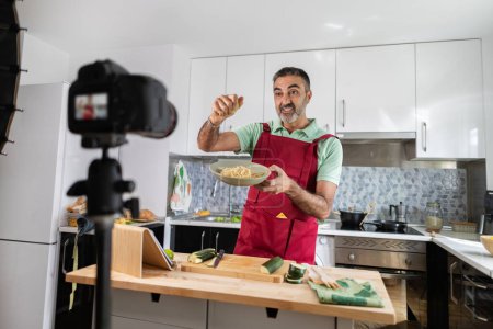 Photo for Adult man recording herself with the camera while cooking for her healthy food blog - Royalty Free Image