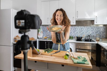 Photo for Adult woman recording herself with the camera while cooking for her healthy food blog - Royalty Free Image