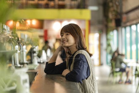 Photo for Japanese Asian woman waits at the bar counter to be served. woman patiently waiting for her order leaning on the counter - Royalty Free Image