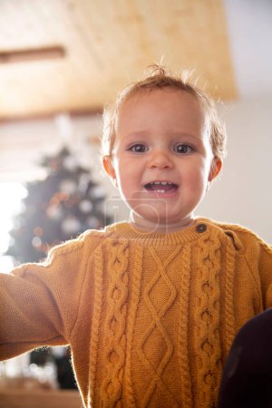 Foto de Primer plano de un niño sonriendo a la cámara mientras su madre toma una foto de él para Navidad con su árbol en el fondo fuera de foco - Imagen libre de derechos