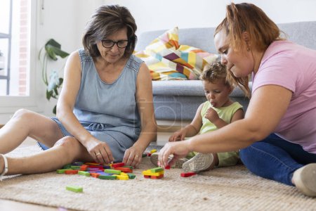 Téléchargez les photos : Famille grand-mère mère mère et fils jouer assis sur le tapis dans leur salon - en image libre de droit