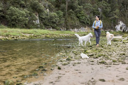 Foto de Joven excursionista paseando por las montañas junto al río con sus perros - Imagen libre de derechos