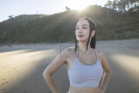 Téléchargez les photos : Jeune femme caucasienne fait du sport sur la plage au lever du soleil, se reposant - en image libre de droit
