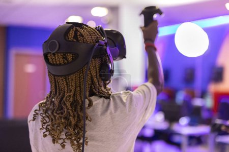 Photo for African American teenager with braids in her hair from behind playing virtual reality games with augmented reality glasses - Royalty Free Image