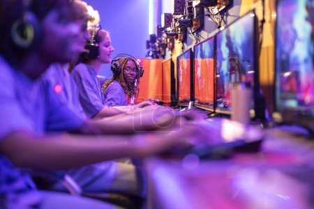Photo for Young group of gamer playing computer in a row with focus on african american teenage girl looking at camera - Royalty Free Image