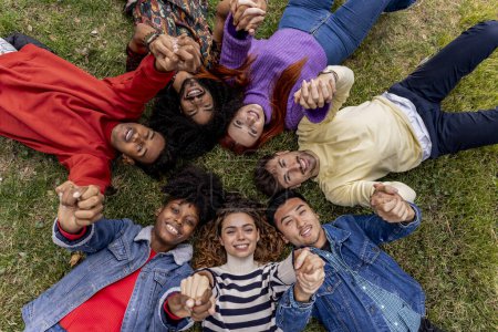 Foto de Un grupo diverso de amigos están tendidos en una hierba en un círculo con sus cabezas juntas y las manos en el aire. no al racismo. solidaridad - Imagen libre de derechos