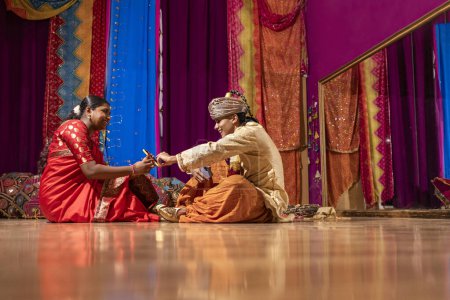 Téléchargez les photos : Couple de jeunes adolescents assis sur le sol se reposant et regardant les téléphones mobiles dans leur cours de danse arabe - en image libre de droit