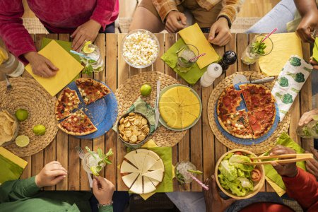 Foto de Familiares o amigos celebrando. comiendo pizza para la cena. Tiro de personas manos en una mesa de madera rústica con varios tipos de alimentos, vista superior. - Imagen libre de derechos
