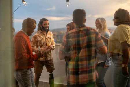 Téléchargez les photos : Groupe multigénérationnel et multiracial de collègues profitant d'une fête en terrasse au coucher du soleil - en image libre de droit