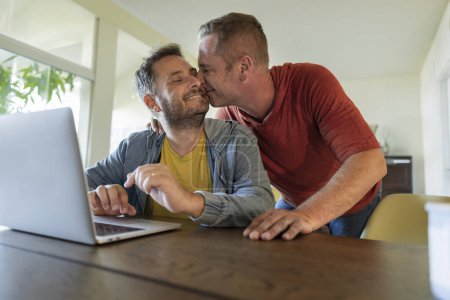 Téléchargez les photos : Couple gay célèbre et embrasse tout en organisant leur voyage de Saint-Valentin devant l'ordinateur portable - en image libre de droit