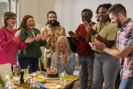 Téléchargez les photos : Famille multi-génération célébrant l'anniversaire de grand-mère à la table avec de la nourriture et du gâteau à la maison - en image libre de droit