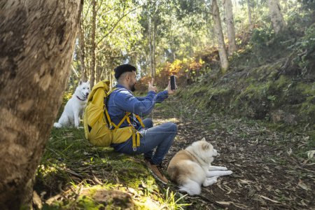 Téléchargez les photos : Jeune homme adulte marchant avec ses chiens dans la forêt faisant un appel vidéo - en image libre de droit