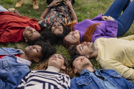 Foto de Grupo de jóvenes multiétnicos que yacen en un círculo sobre la hierba con los ojos cerrados - Imagen libre de derechos
