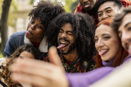 Foto de Detalle de cerca en joven adulto afroamericano hombre con lengua gesto bromas con su grupo de amigos mientras toma una selfie - Imagen libre de derechos