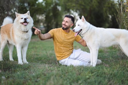 Téléchargez les photos : Homme souriant assis sur le sol à l'extérieur pointant le chemin avec ses chiens - en image libre de droit
