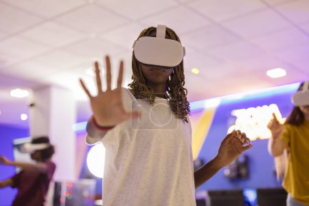 Photo for Portrait of african american girl gamer with braids wearing virtual reality glasses touching with open hand to camera - Royalty Free Image