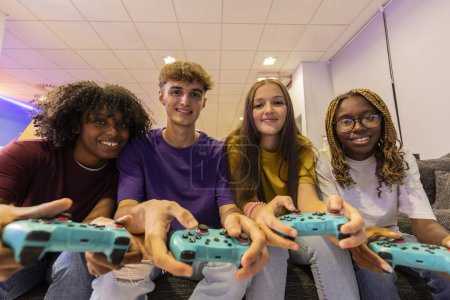 Foto de Grupo de jugadores jugando consola - plano frontal del grupo de amigos adolescentes multirraciales mirando a la cámara jugando consola de videojuegos con controladores - Imagen libre de derechos