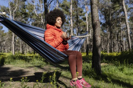 Téléchargez les photos : Femme afro-américaine assise avec du thé chaud dans un hamac - en image libre de droit