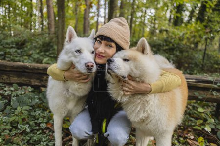 Foto de Retrato de mujer joven de vacaciones con sus perros mirando a la cámara mientras les da amor y abrazos - Imagen libre de derechos