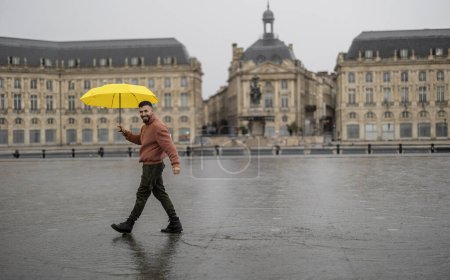 Foto de Hombre con paraguas amarillo turismo en Bourdeux en un día nublado y lluvioso, pero con una actitud positiva - Imagen libre de derechos