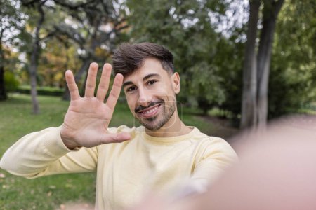 Foto de Selfie de hombre joven mirando la cámara y saludando con la mano - Imagen libre de derechos