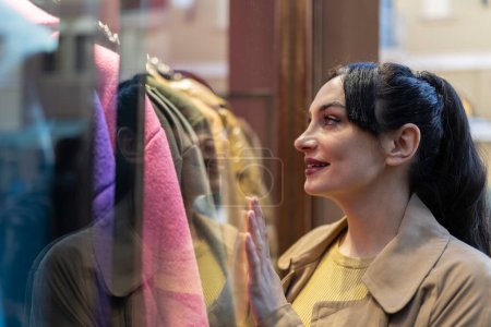 Téléchargez les photos : Femme regardant un affichage de vêtements reflétés dans le verre avec sa main soutenue- désir et shopping - en image libre de droit