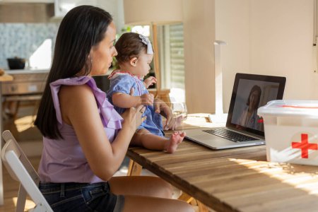 Téléchargez les photos : Mère avec sa fille assise à la table parlant au médecin pédiatre avec l'ordinateur dans leur rendez-vous virtuel en ligne - en image libre de droit