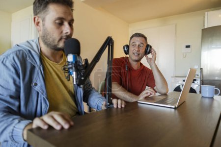 Téléchargez les photos : Créateurs de contenu masculin, présentateur streaming son podcast sur un ordinateur portable avec écouteurs et microphone. Blogueur masculin enregistrement de la voix à la radio - en image libre de droit