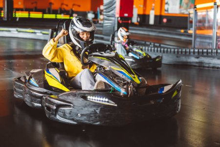 Photo for Excited asian teenage woman raising fist high at kart race competition giving a shout overtaking her rivals with the car - Royalty Free Image