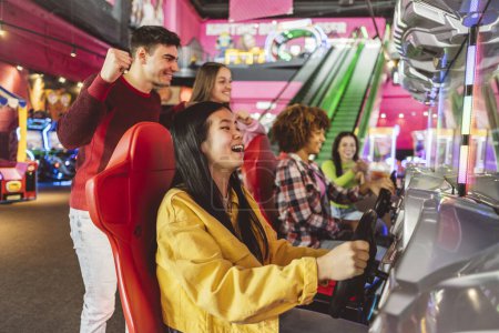 Photo for Asian woman playing with her multiethnic friends in racing games in an arcade game center while her friends celebrate and cheer - Royalty Free Image