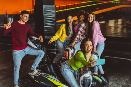 groupe d'amis adolescents multiraciaux prenant un selfie avec le téléphone sur la piste de kart