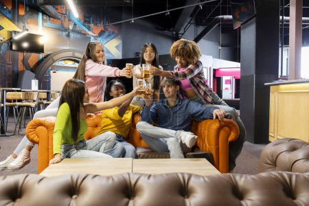 Téléchargez les photos : Groupe de jeunes amis multiraciaux trinquer avec leurs verres de bière dans un lieu de loisirs célébrant leur réunion le week-end - en image libre de droit