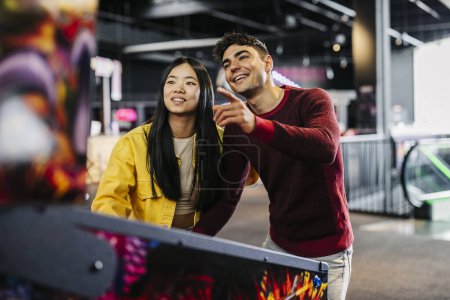 multiracial couple friends playing pinball in arcade amusement game room