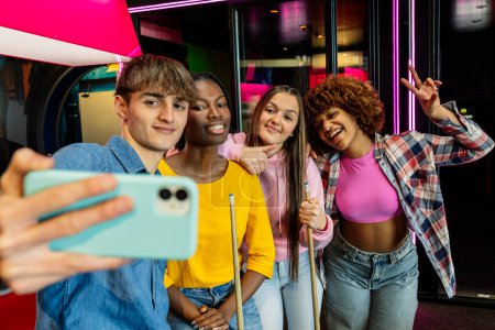 Téléchargez les photos : Selfie d'amis multiraciaux dans la salle d'arcade jouant au billard - en image libre de droit