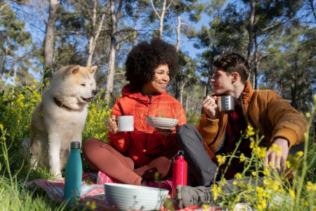 Photo for Multiracial couple with their dog on picnic in nature. - Royalty Free Image