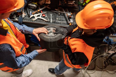 Téléchargez les photos : Vue d'en haut des collègues de maintenance passant une roue pour la réparation de kart - en image libre de droit