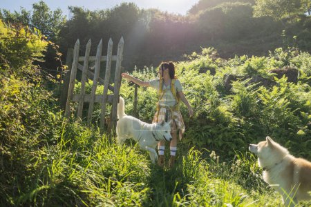 Foto de Mujer mochilera con sus perros abriendo la puerta de la cerca en el campo para continuar a lo largo del sendero - Imagen libre de derechos