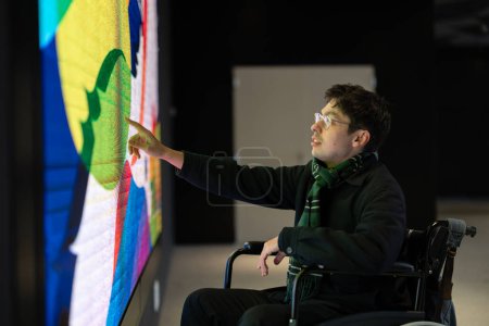 Téléchargez les photos : Homme en fauteuil roulant touchant une interface de pointe avec des éléments futuristes. Interaction manuelle avec les projections holographiques sur l'écran LED - en image libre de droit