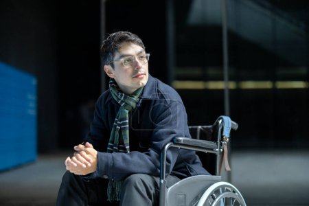 junger Mann im Rollstuhl nachdenklich, mit einem Hintergrund von Gebäuden reflektieren