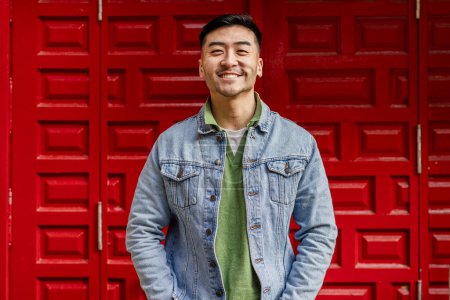 Téléchargez les photos : Portrait de asiatique homme regardant caméra sur fond rouge - en image libre de droit