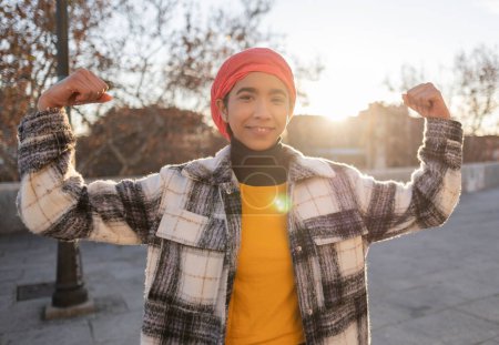 young latin woman with a pink scarf on her head and arms flexed raising awareness about breast cancer