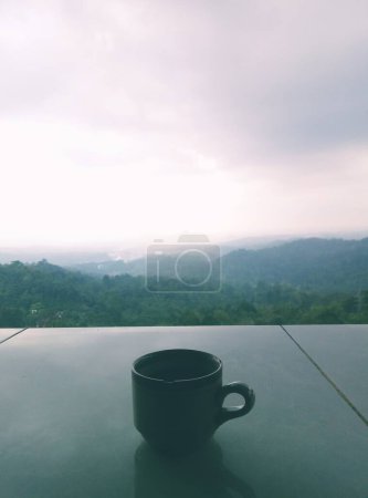 Retrato de taza de café en la mesa de cerámica con el hermoso paisaje natural de montañas, colinas o bosques en el fondo.