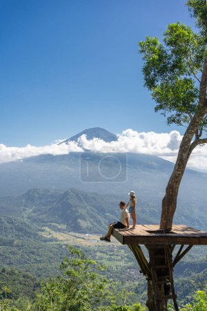 Foto de Padre e hija turistas disfrutando de viajar por la isla de Bali, Indonesia. Se encuentra en la ubicación de la foto en el árbol con vista a la montaña Agung - Imagen libre de derechos