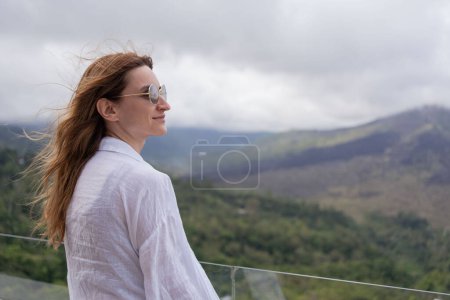 Photo for Young woman traveler looking at Batur volcano. Indonesia, while stand in cafe terrace. - Royalty Free Image