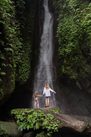 Foto de Familia en una cascada tropical. Una mujer y un niño en una hermosa cascada. Vacaciones en una isla tropical. Pareja viajera en la cascada. Familia de vacaciones en Bali - Imagen libre de derechos